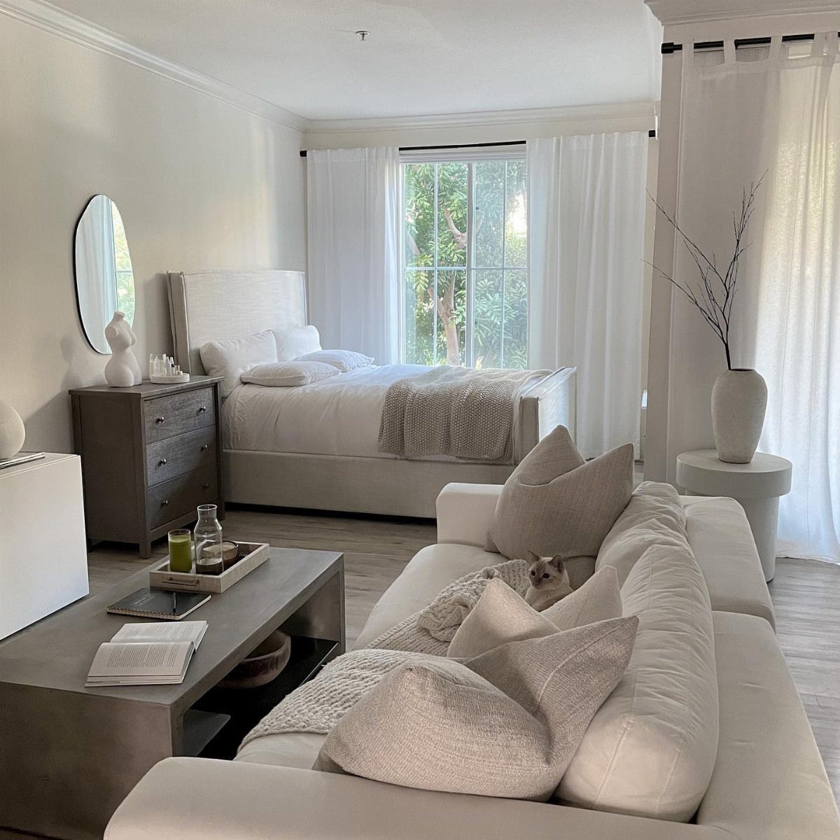 Bright studio room with white furniture, neutral tones, and large sunlit windows.