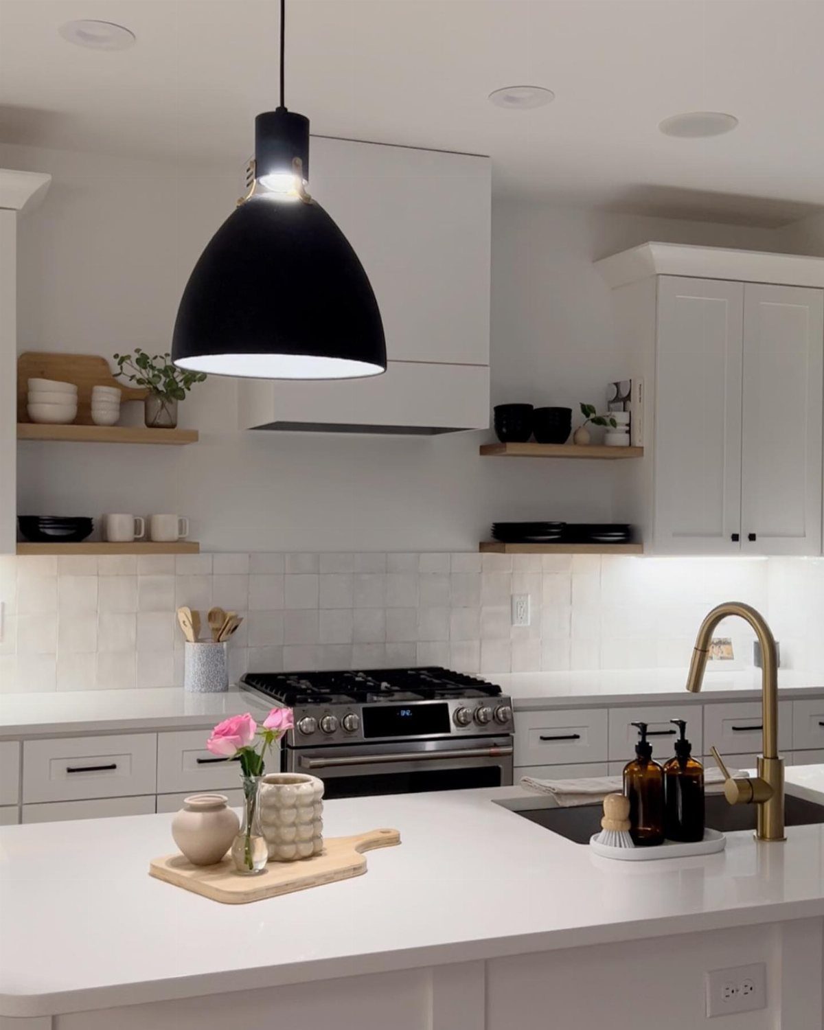 Modern white kitchen featuring light wood open shelving with decorative bowls and plants.