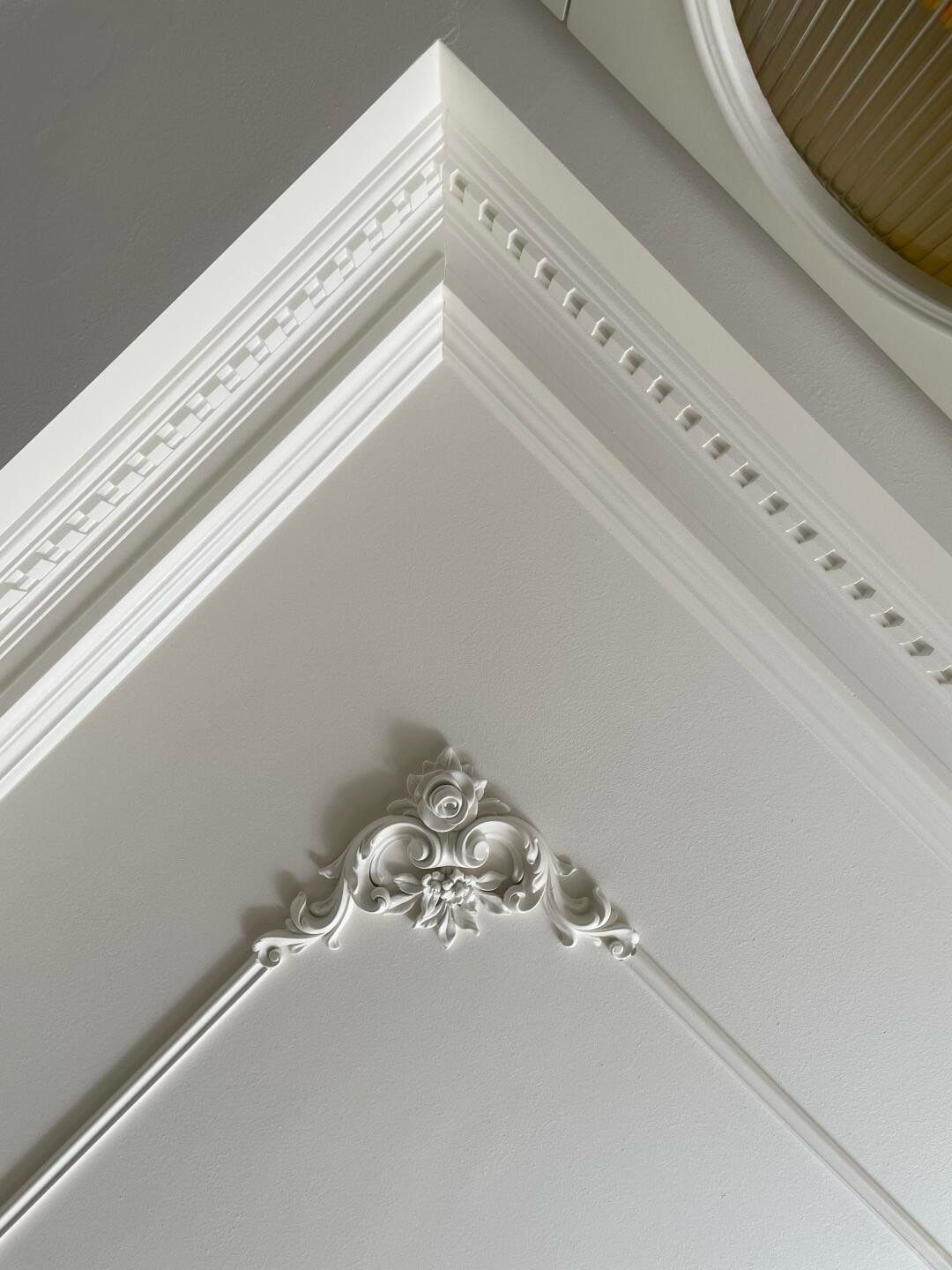 White decorative crown molding and ornate plaster ornament on a light grey ceiling.