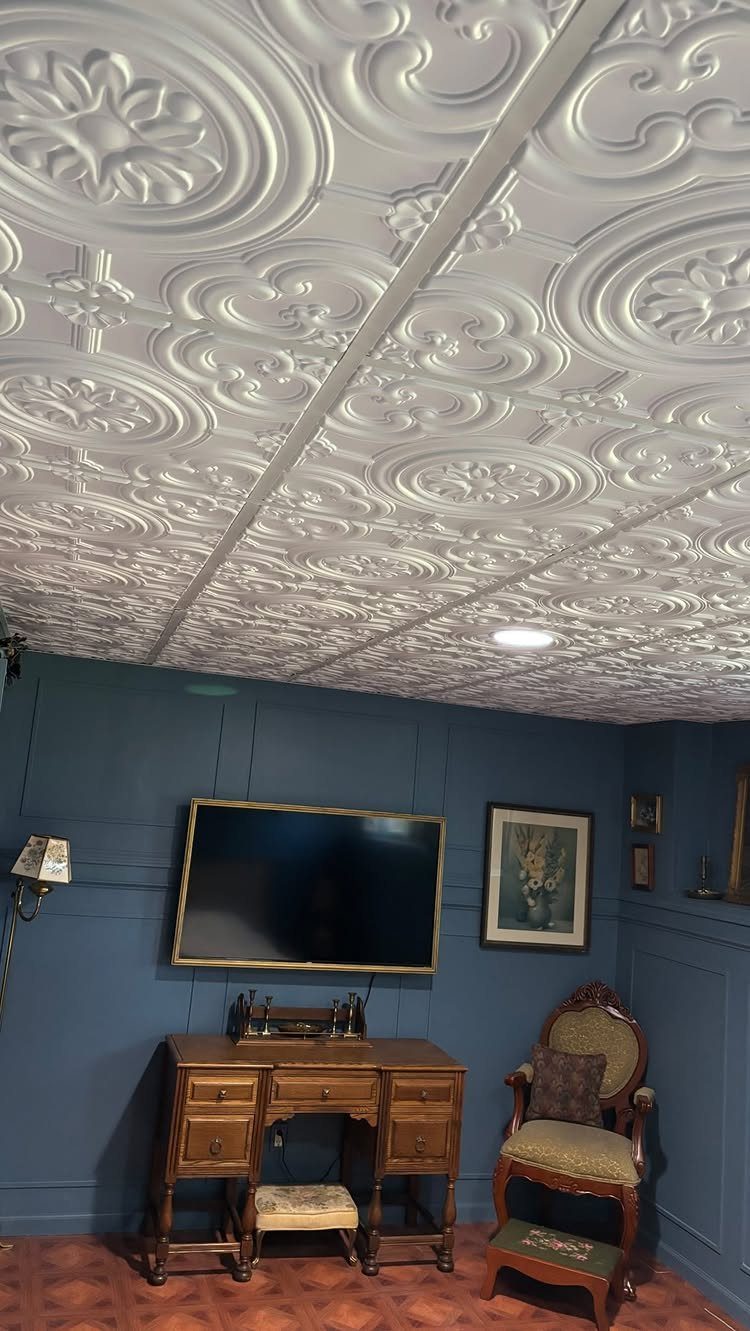 White ornate patterned ceiling tiles above a blue room with vintage furniture.