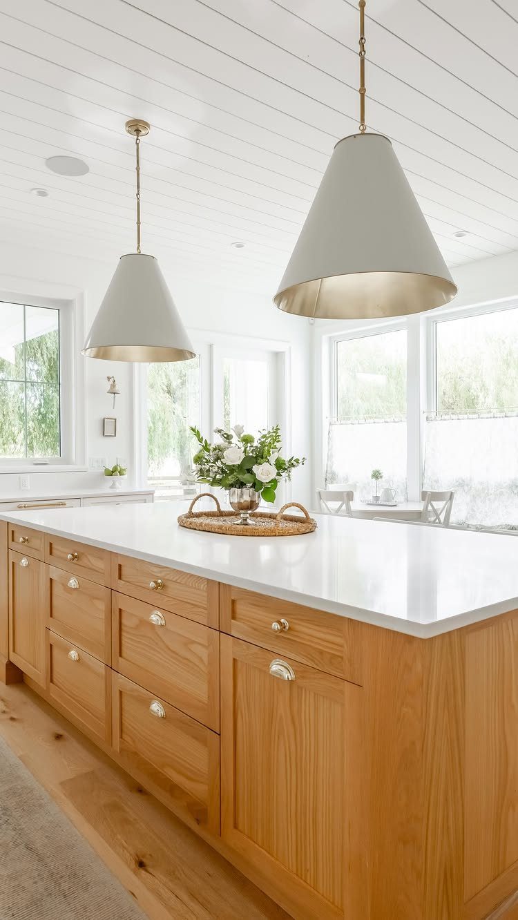 Wooden kitchen island with white countertop and white conical pendant lights under shiplap ceiling