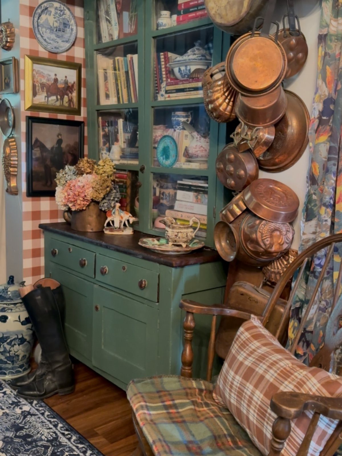 Copper pots and pans hanging next to a green vintage display cabinet.