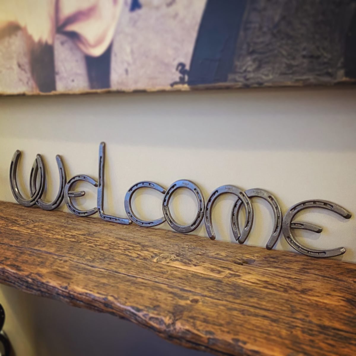 Metal horseshoes welded to spell Welcome resting on a rustic wooden shelf
