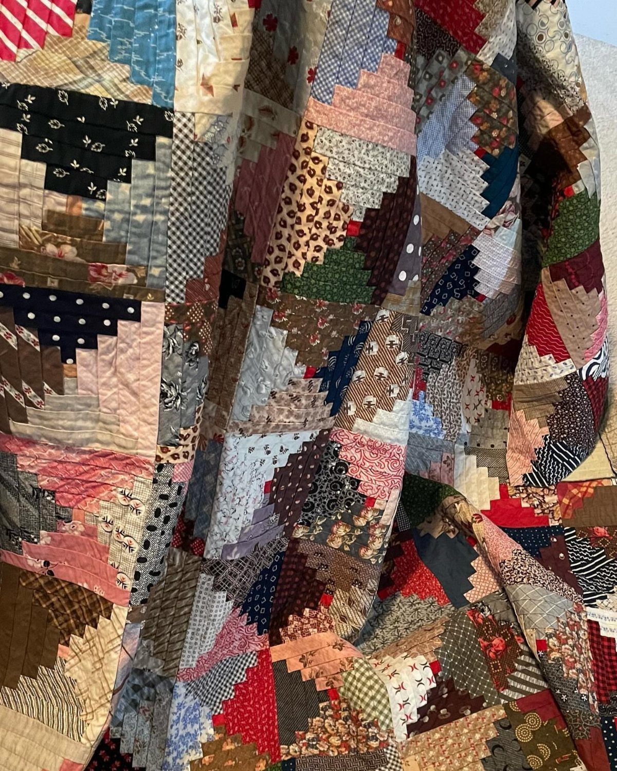 Multi-colored patchwork quilt with various fabric patterns draped in soft folds.