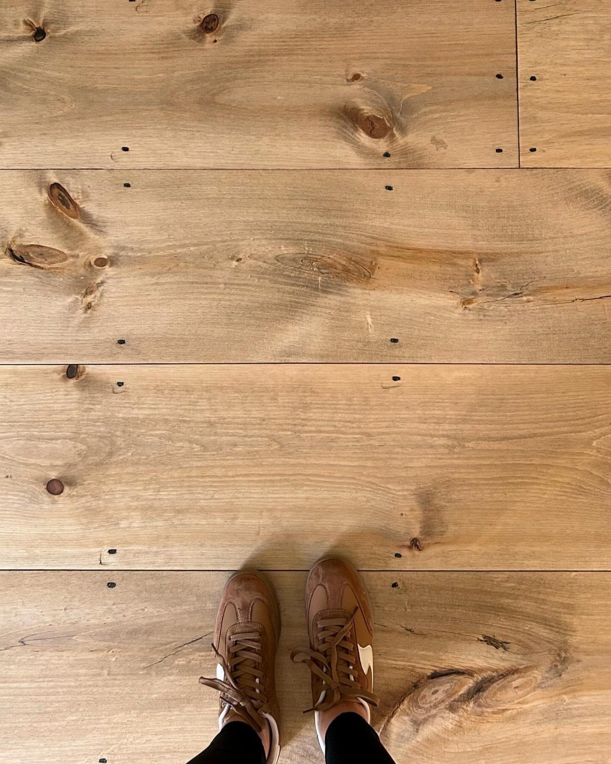Light brown timber floorboards with visible knots and a person wearing brown sneakers.
