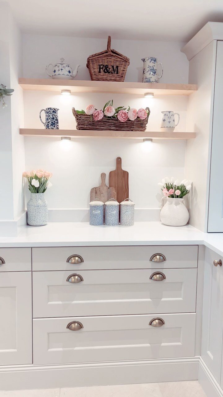 White kitchen cabinets and countertop with natural wood floating shelves and floral decor.