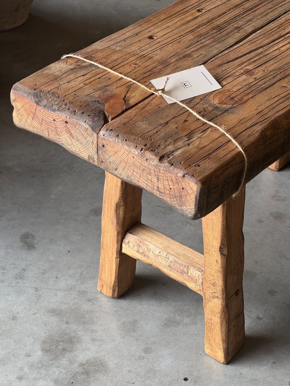 Weathered wooden bench made of thick rustic timber planks on a concrete floor