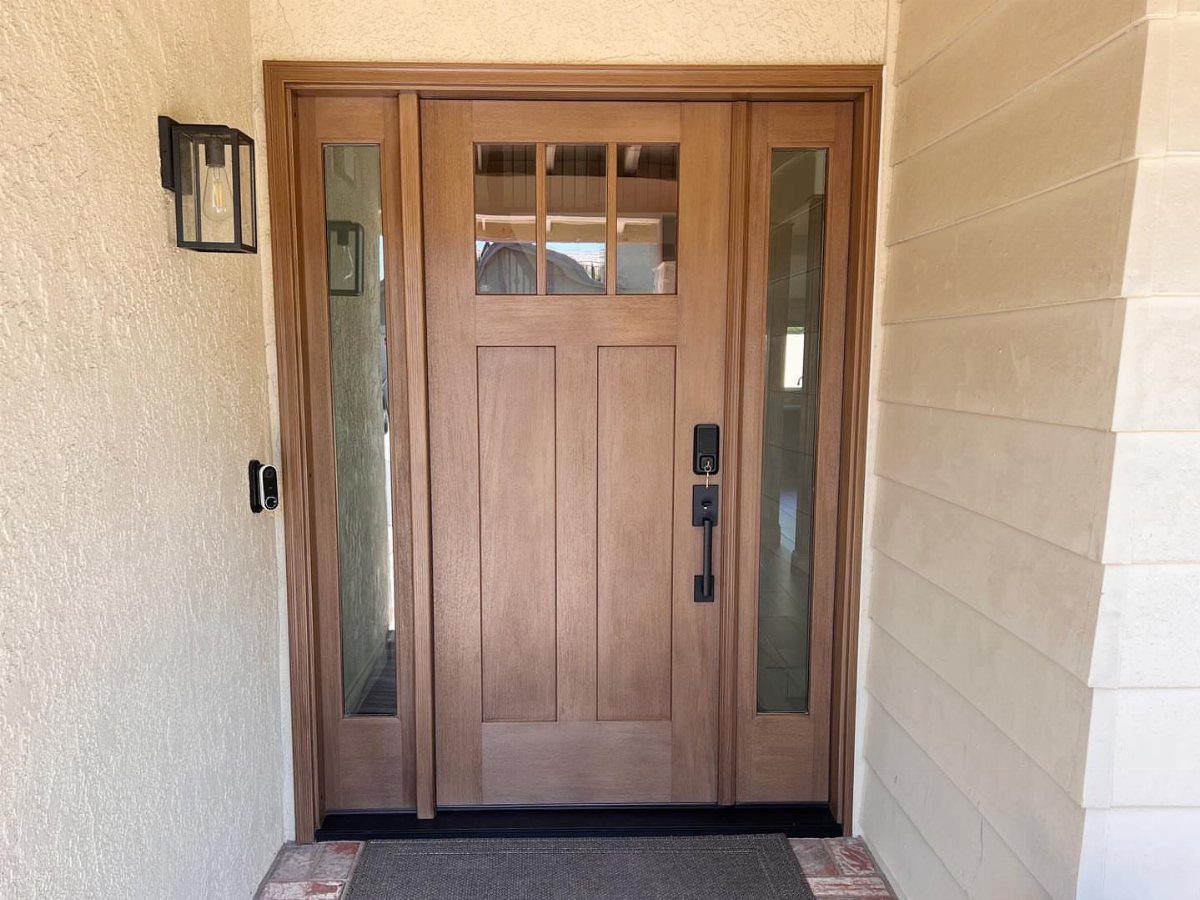 Natural wood front door with sidelights and a black outdoor wall lantern.