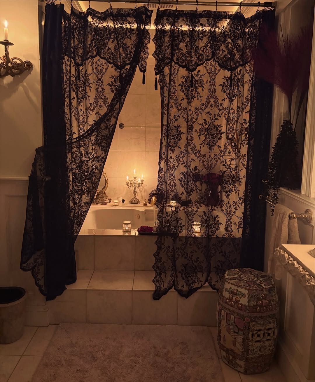 Black lace curtains and valance draped over a white tiled bathtub area.