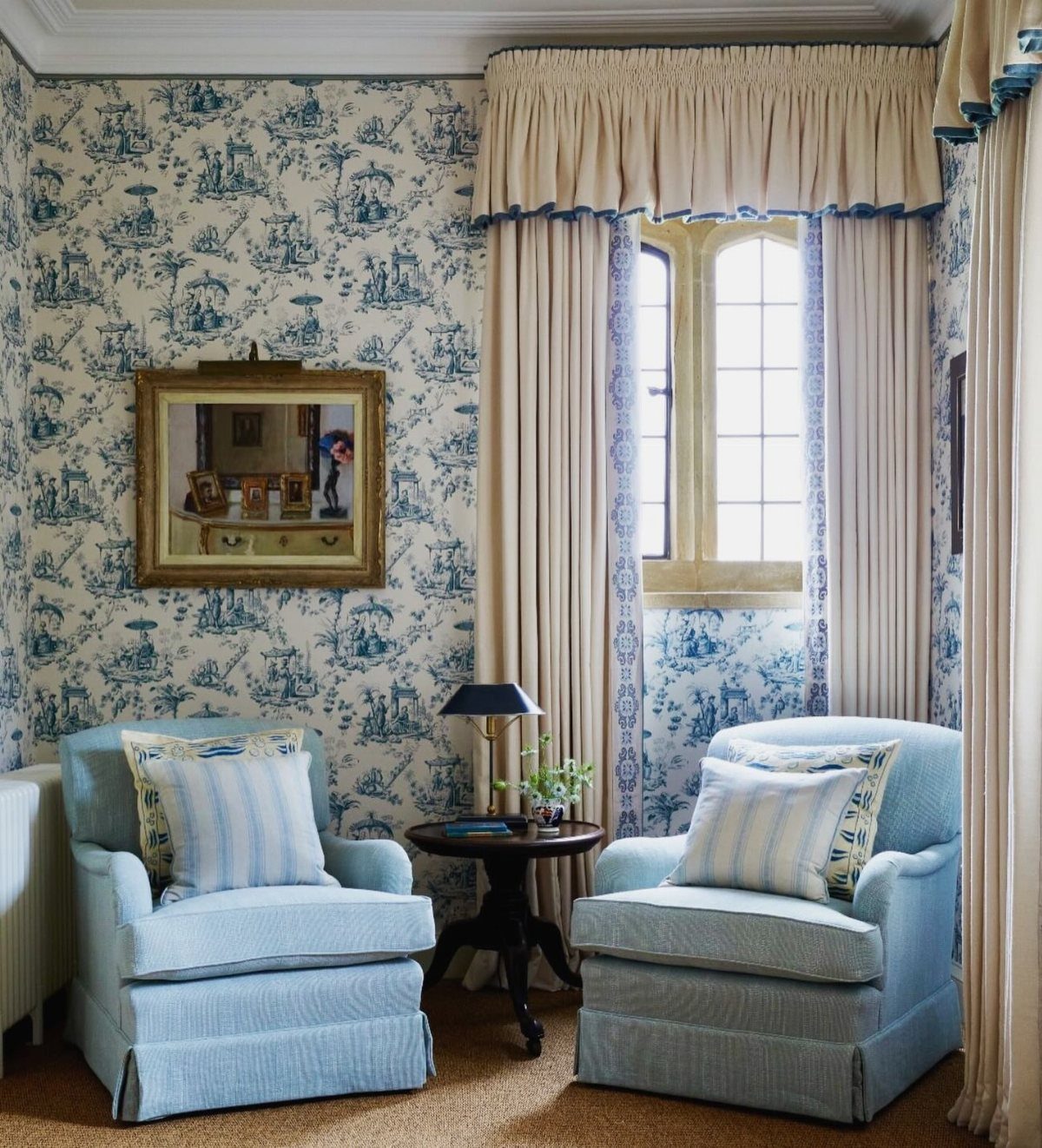 Cream curtains and valance in a room with blue toile wallpaper and armchairs.
