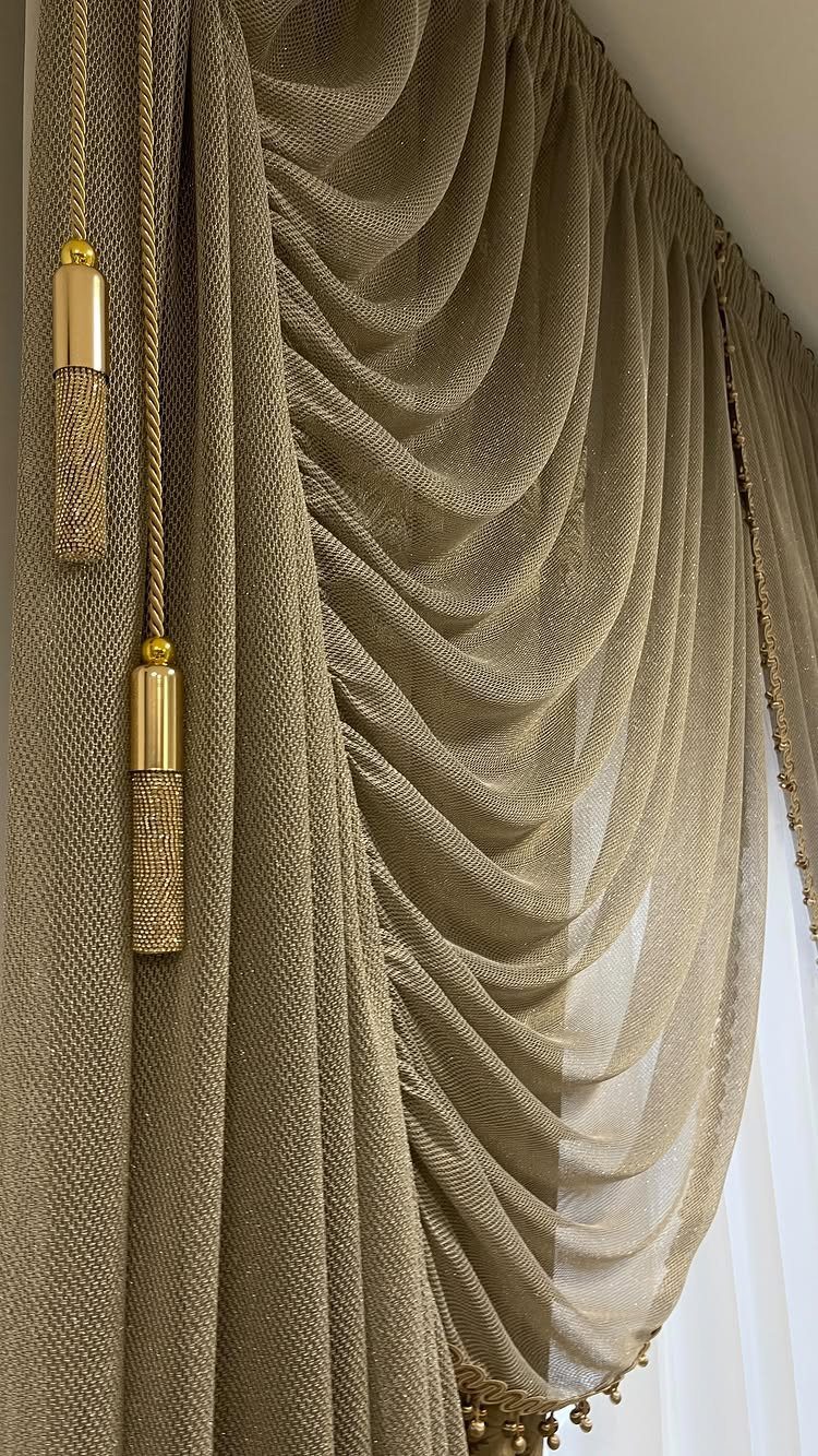 Gold textured curtains and a draped valance with decorative tassels over a window.