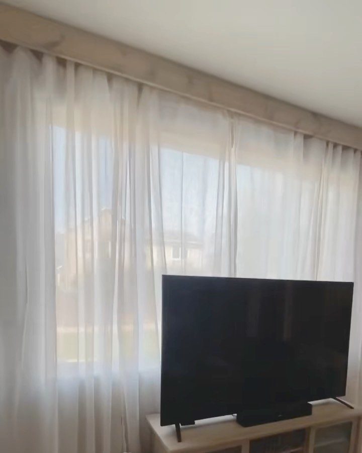 White sheer curtains with a light wood valance behind a black television.
