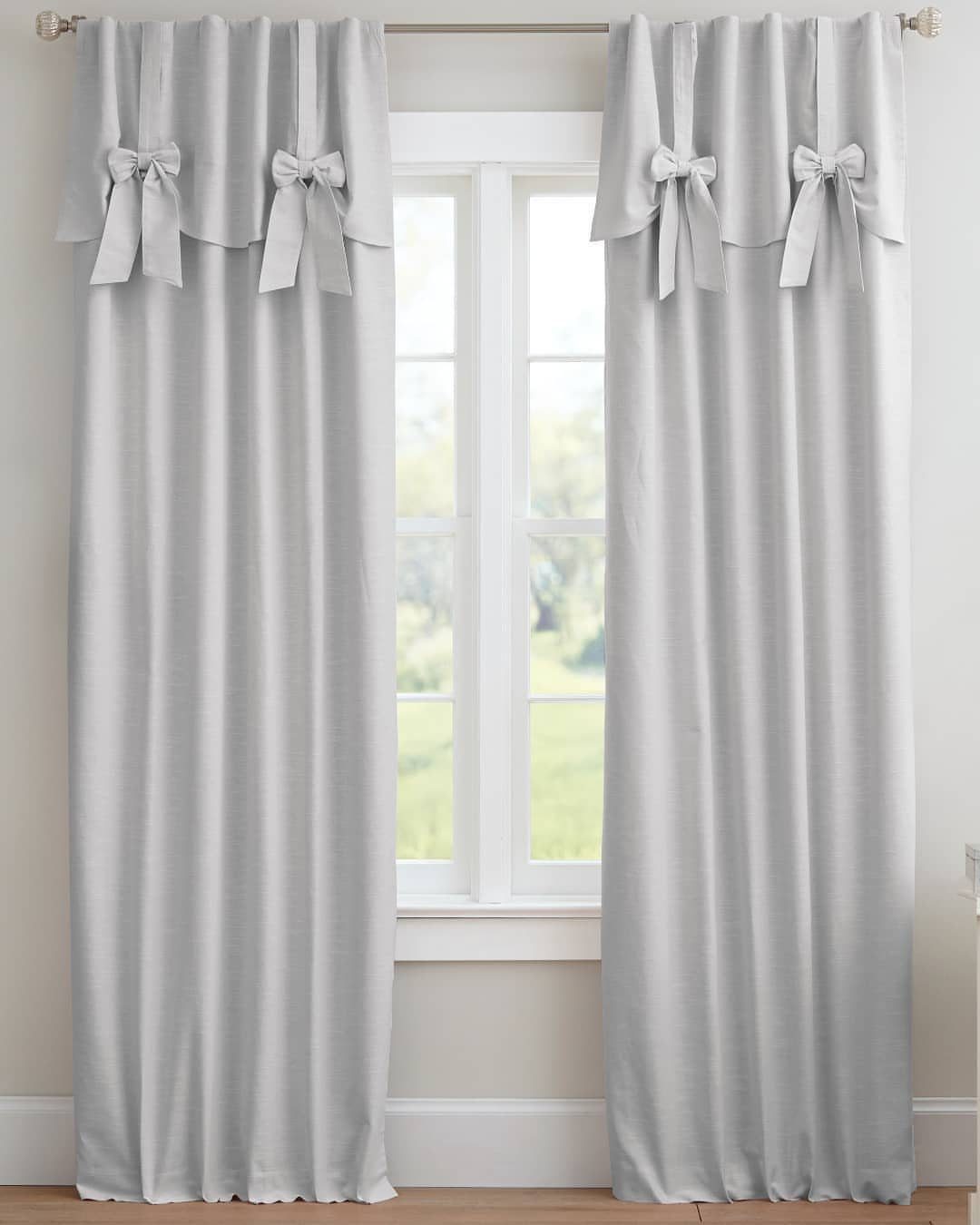 Light grey curtains and valances with bows hanging over a white window