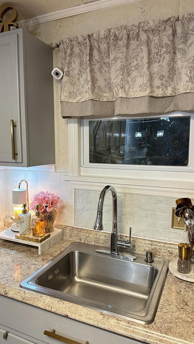 Beige floral valance hanging over a small kitchen window above a stainless steel sink