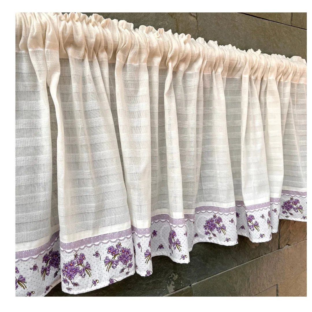 White gathered fabric valance with purple floral embroidery on a stone wall.