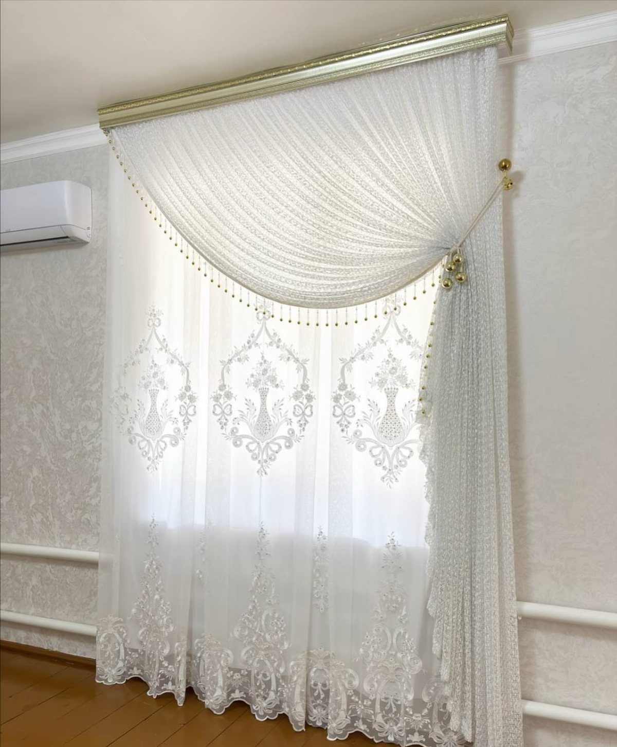 White lace curtains with a draped valance and gold beaded trim on a window