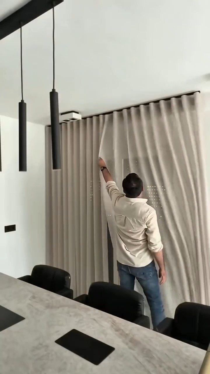 Beige wave-fold curtains mounted to a ceiling track in a modern interior room.