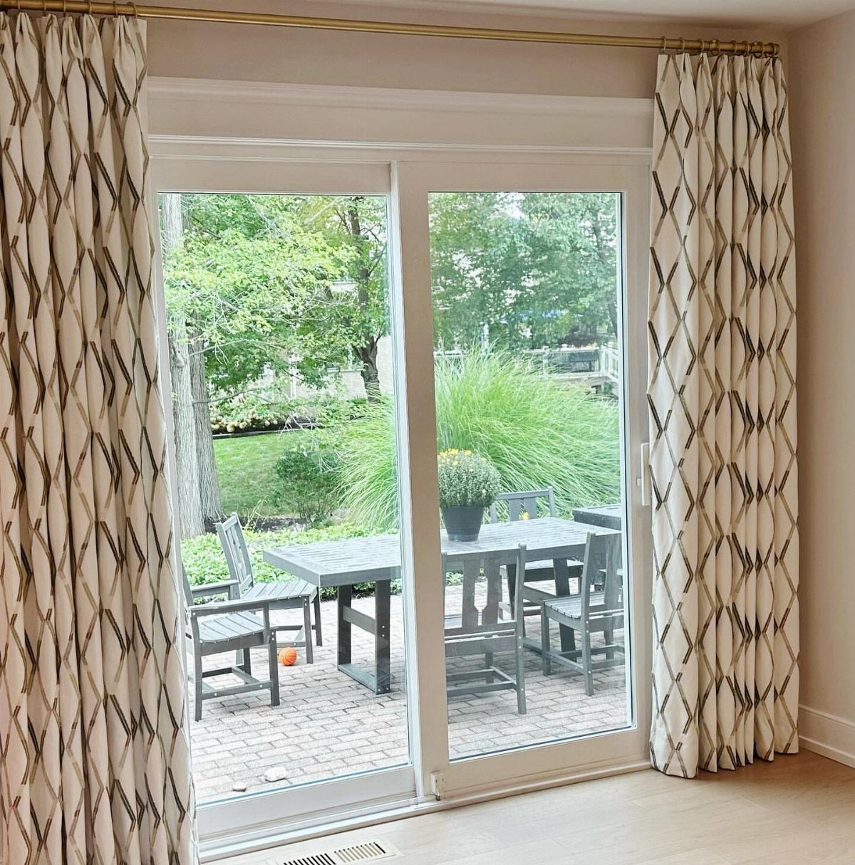 Patterned white curtains framing a sliding glass door leading to a patio garden