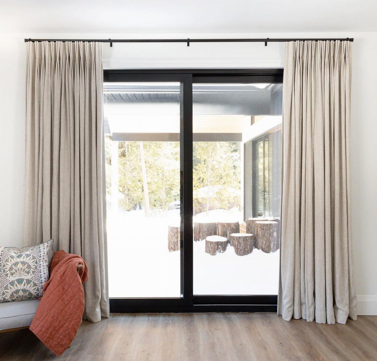 Beige curtains framing a black sliding glass door leading to a snowy yard