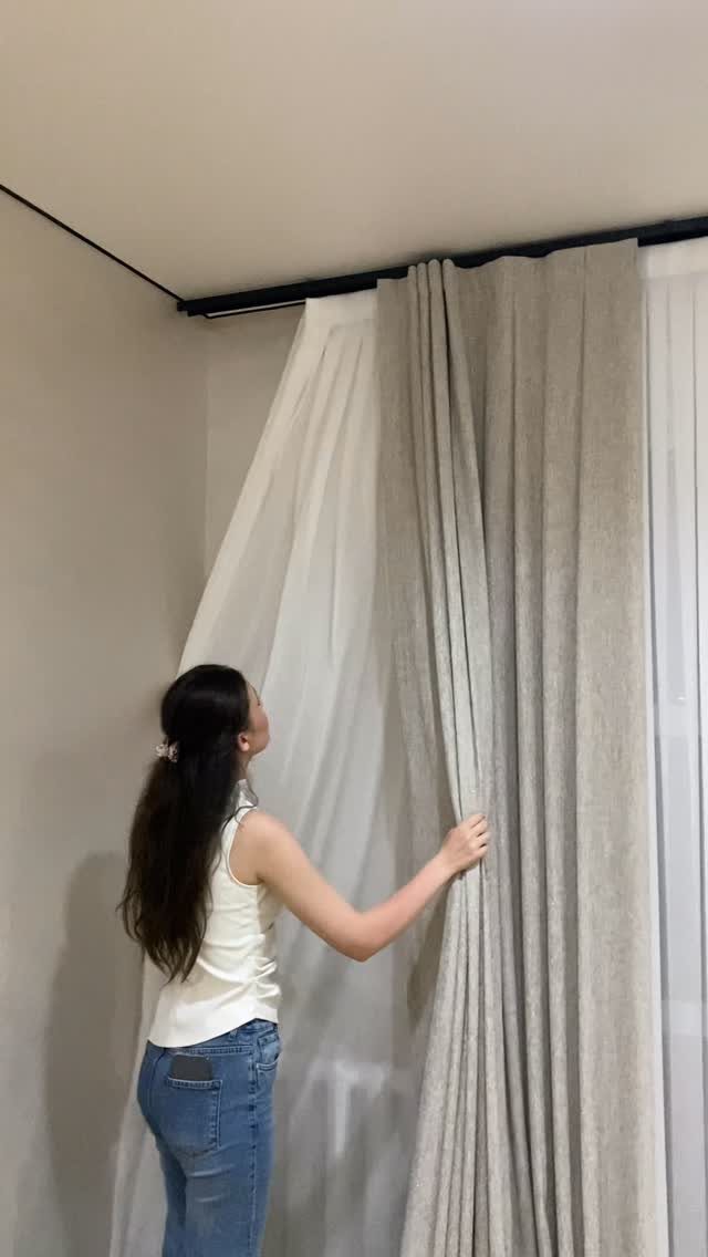Woman adjusting heavy beige drapes over white sheer curtains on a black rod