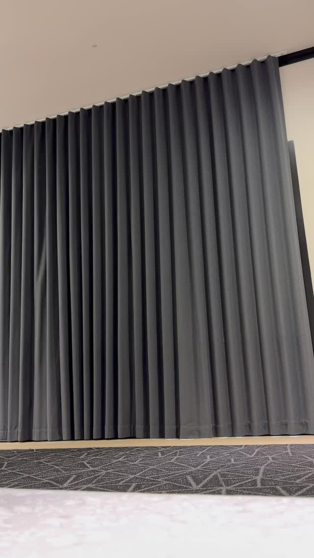 Grey pleated curtains hanging from a black rod over a patterned carpet floor