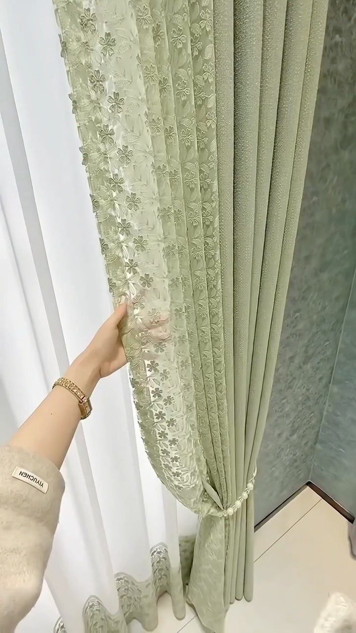 Sage green lace and fabric curtains hanging against a matching sage green wall.