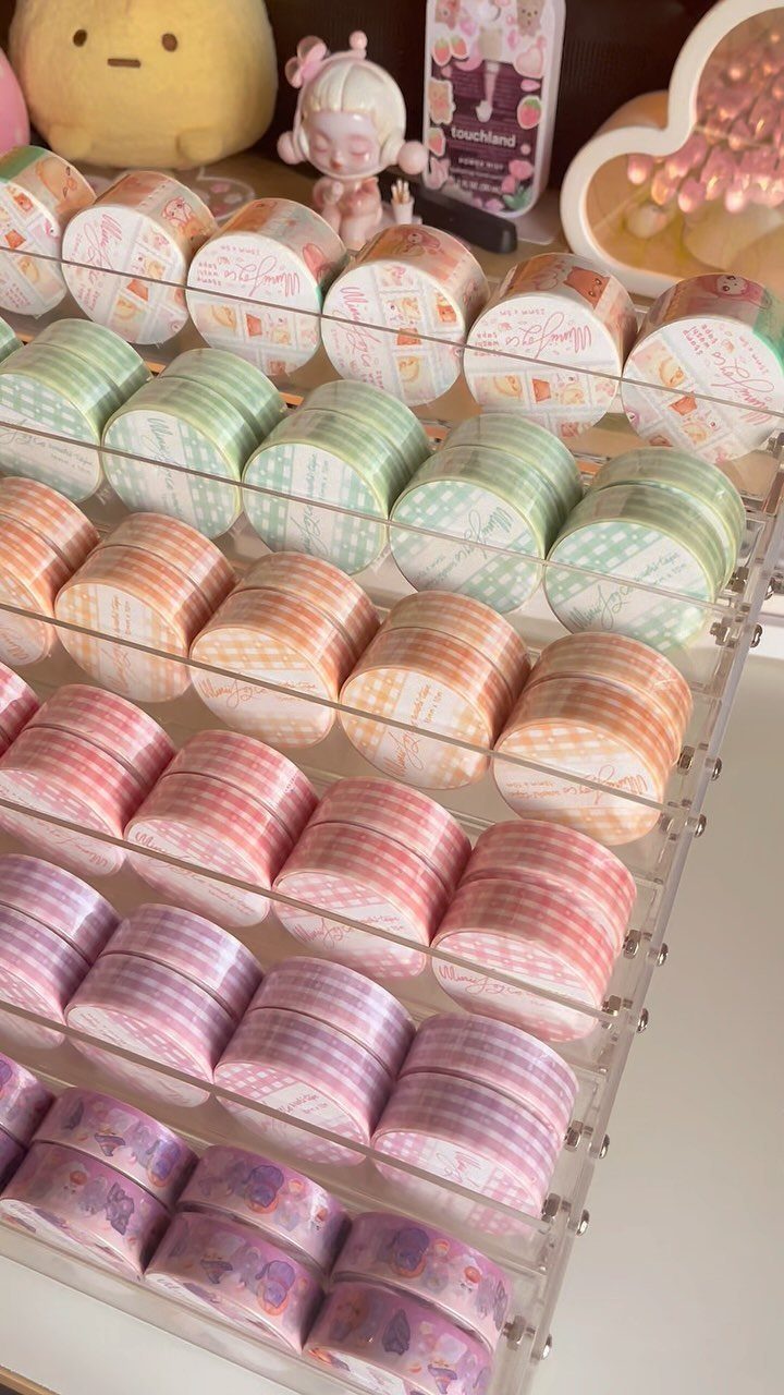 Pastel washi tape rolls organized in a clear acrylic rack on a desk.