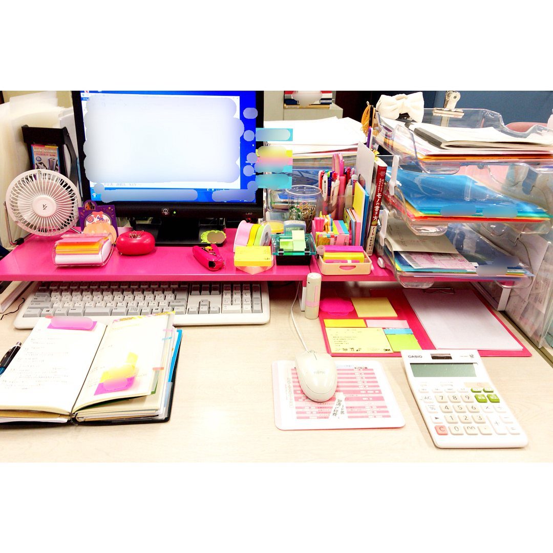 Colorful office supplies and a pink monitor riser on a white office desk
