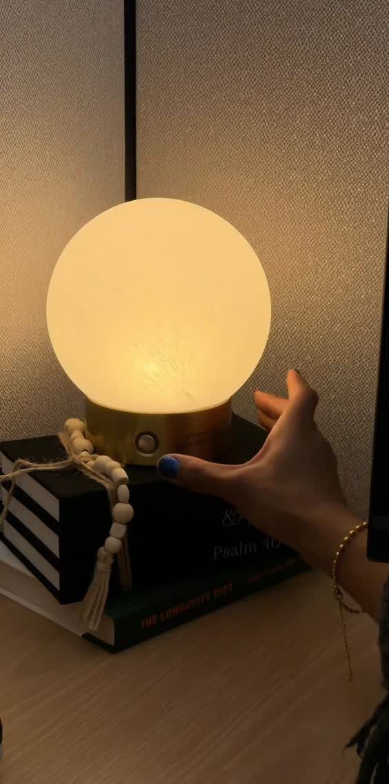Glowing spherical white lamp with gold base sitting on a stack of books.