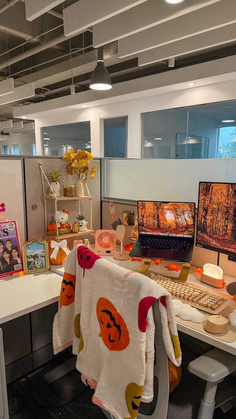 Decorated office cubicle with autumn themes, pumpkin blanket, and fall foliage on desk.