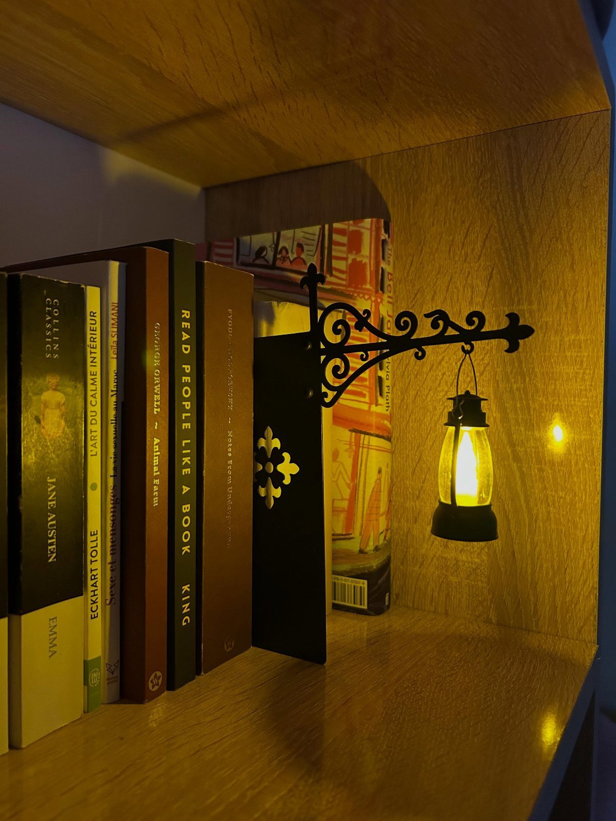 Black metal street lamp bookend holding books on a wooden shelf with glowing light.