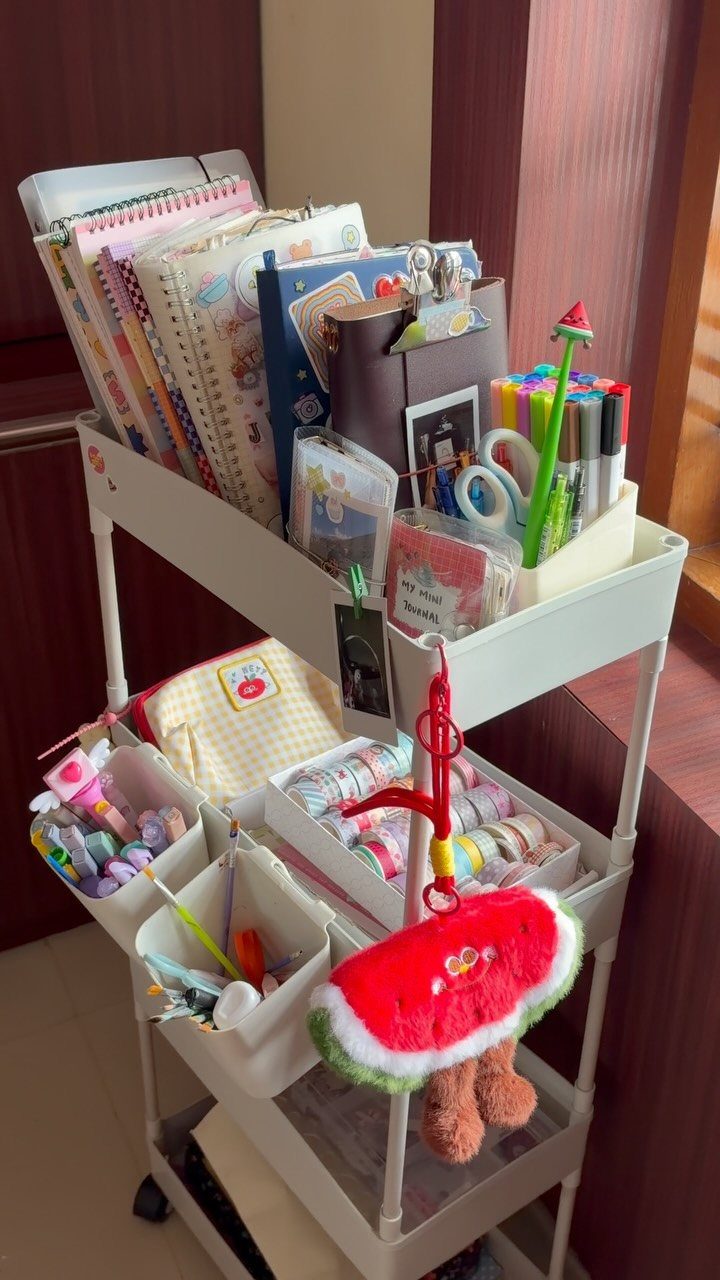 White rolling cart organized with colorful notebooks, markers, and cute stationery supplies.