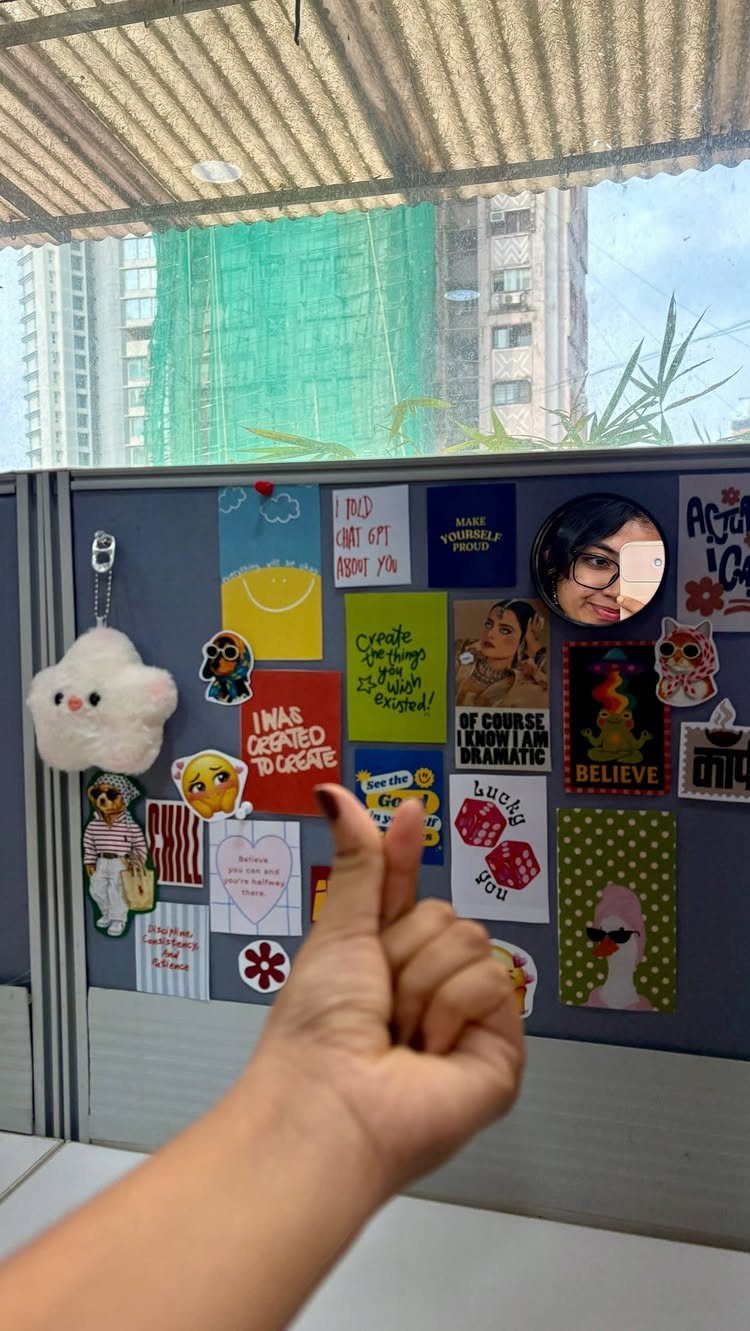 Decorated grey cubicle wall with colorful stickers, photos, and a white plush charm.