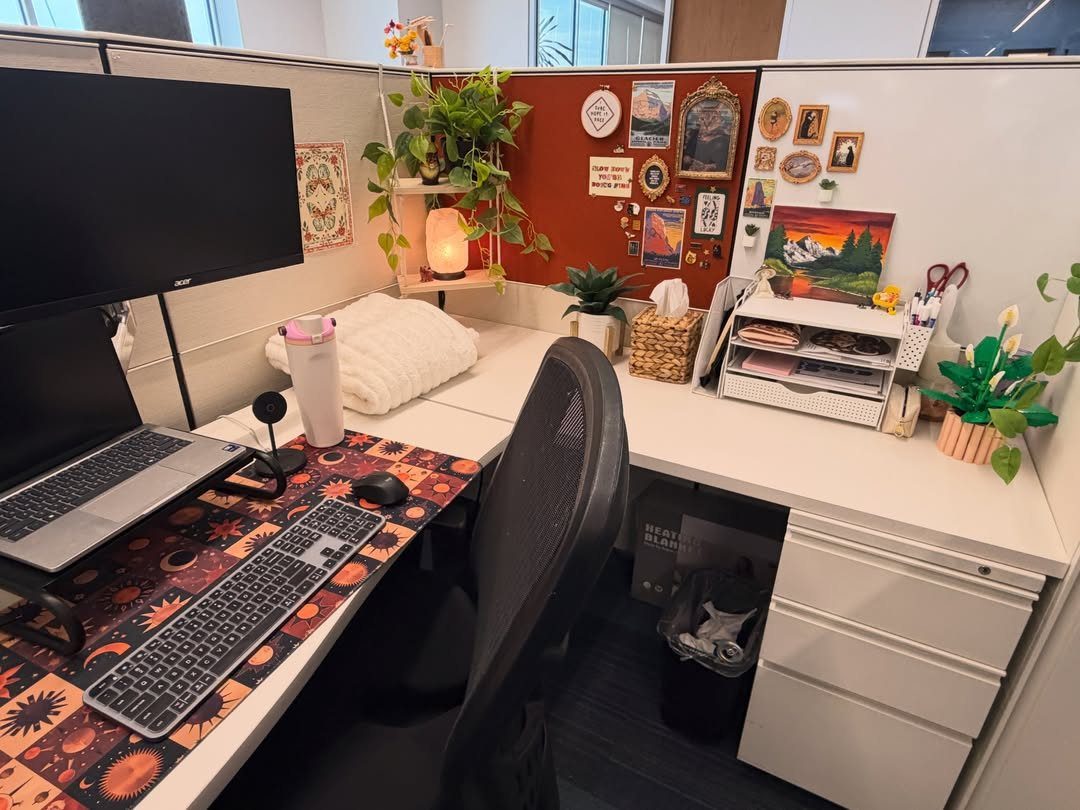 Decorated office cubicle with plants, photos on a red corkboard, and orange desk mat.
