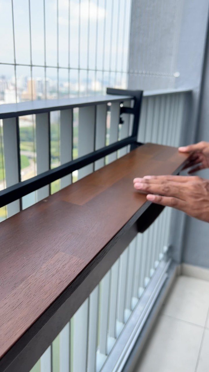 Wooden folding balcony table attached to a black metal railing overlooking a city.