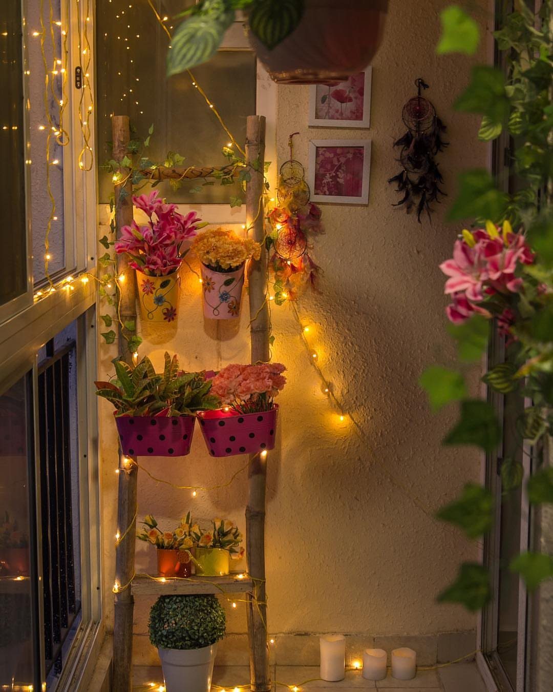 Wooden decorative ladder holding colorful potted plants and draped with warm string lights.