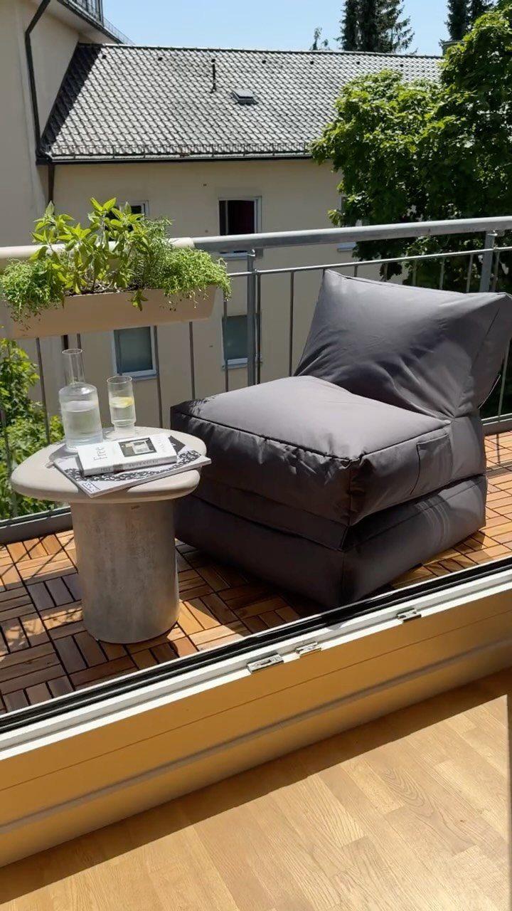 Grey low-profile floor cushion and concrete side table on a small tiled balcony.