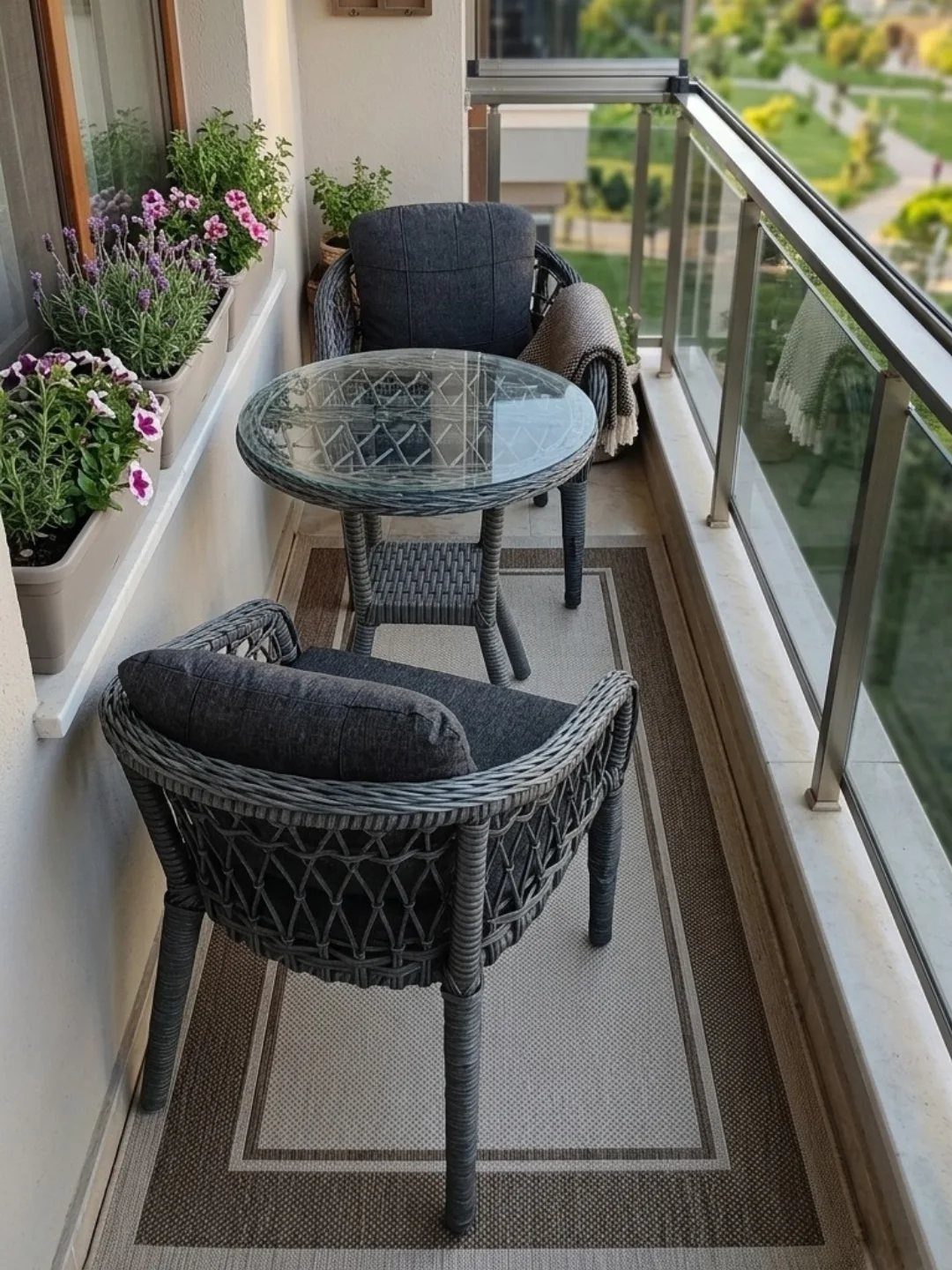 Grey wicker furniture and a rectangular outdoor rug on a small, sunny balcony.