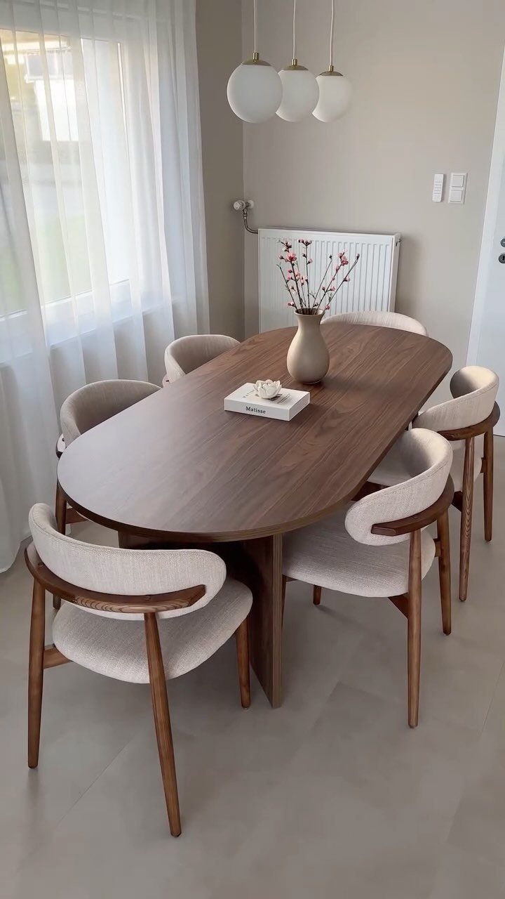Oval dark wood dining table with curved beige mid-century modern chairs in a bright room