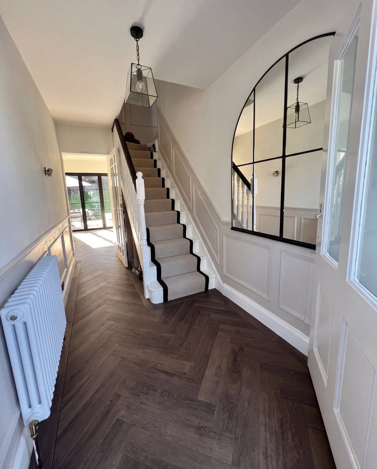 Dark brown herringbone wood flooring in a bright hallway with white wainscoting walls.