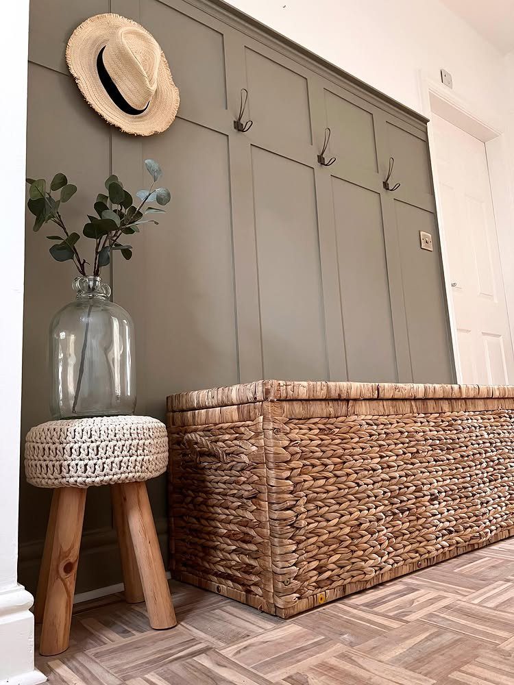 Grey-green board and batten wall with a wicker chest and straw hat.