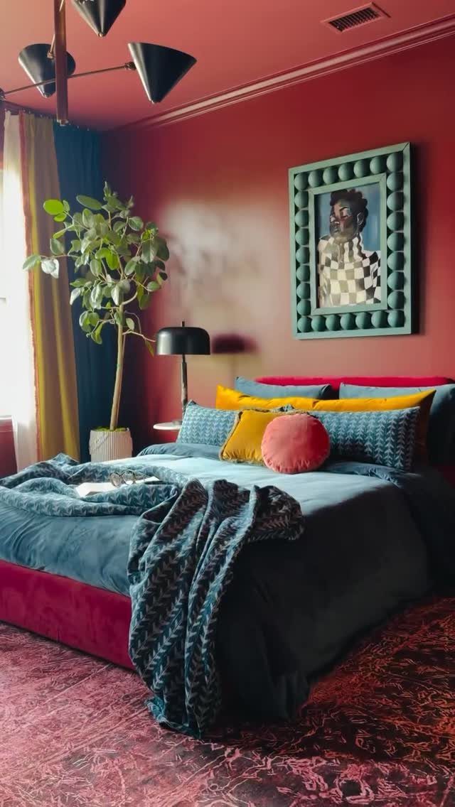 Deep red painted bedroom wall with a bed and teal framed artwork.