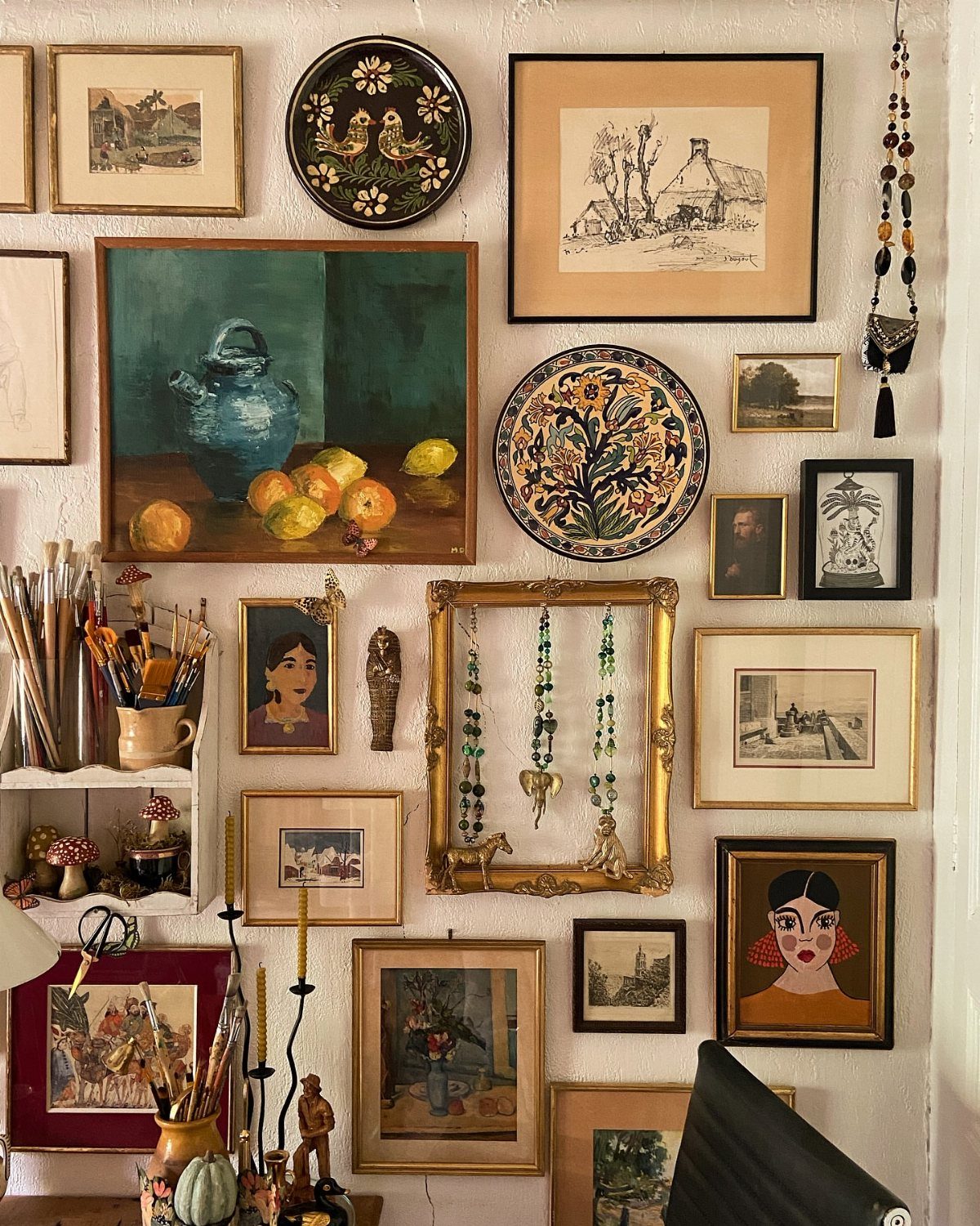 Gallery wall featuring various framed artworks, decorative plates, and jewelry on a white wall.