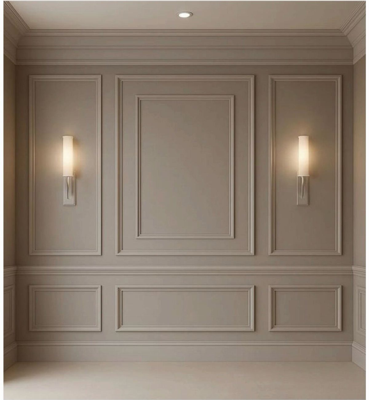 Taupe wall with elegant picture frame molding and two glowing wall sconces.
