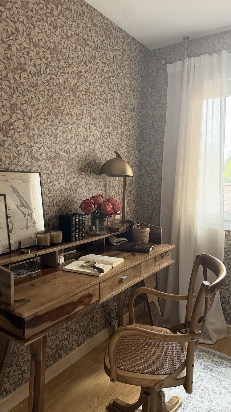Floral patterned wallpaper on a wall behind a wooden desk and chair.