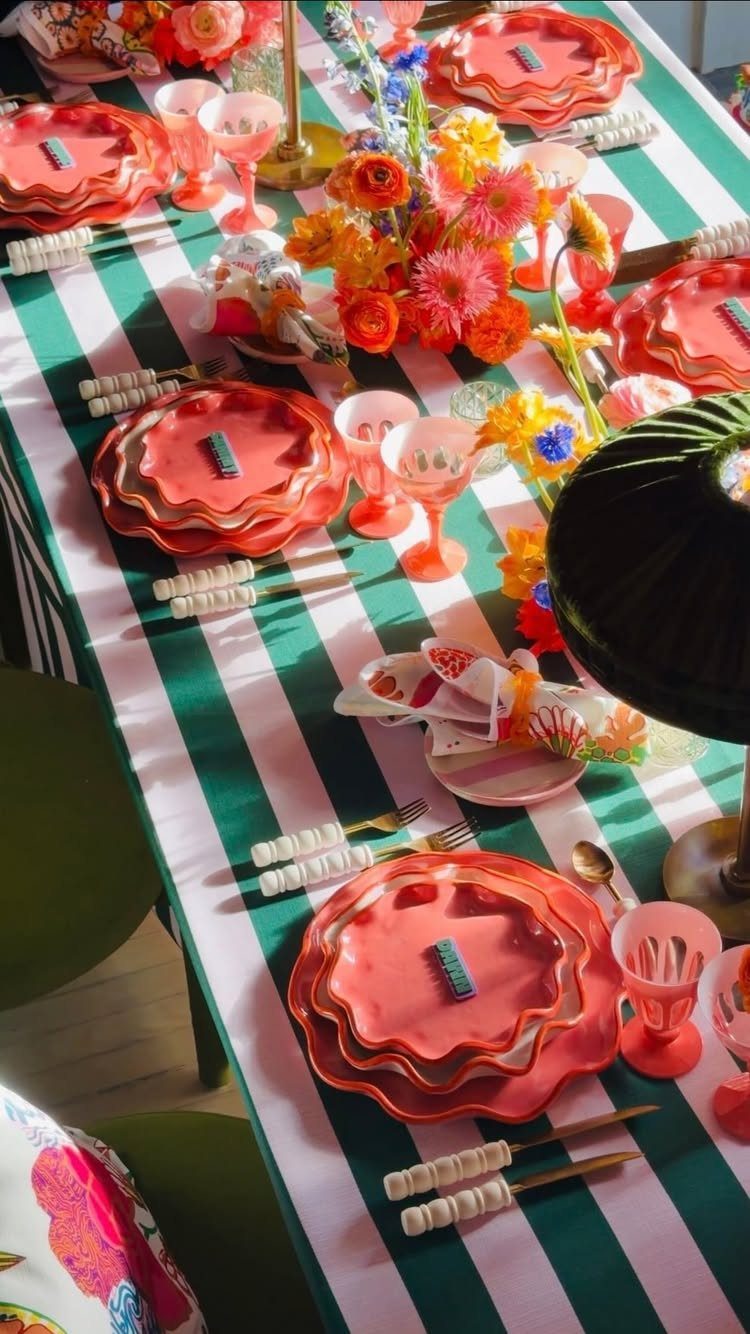 Bright orange plates and glassware on a green striped tablecloth with floral centerpieces.