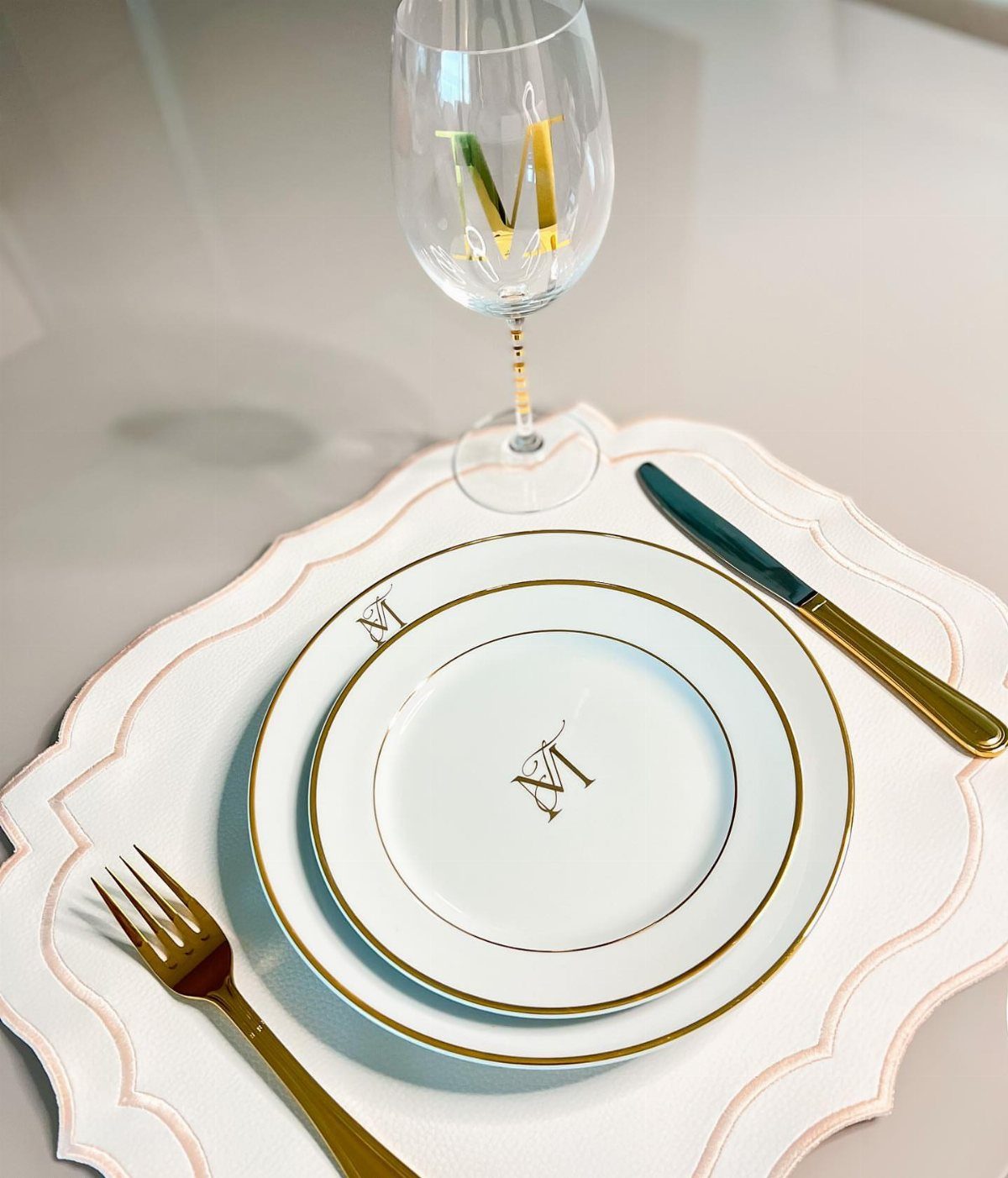 Layered white and gold monogrammed plates on a white scalloped charger plate.
