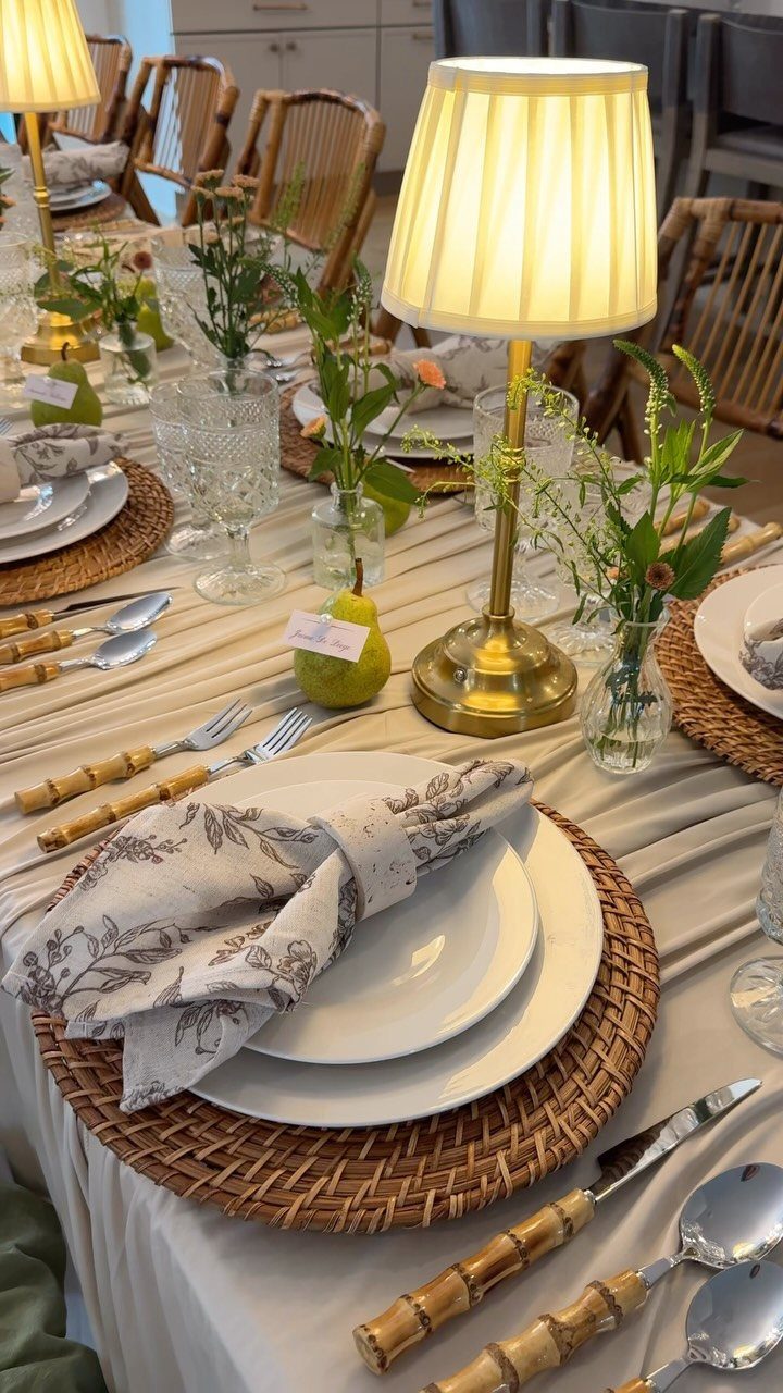 Elegant dinner table setting with rattan placemats, white plates, and gold table lamps.