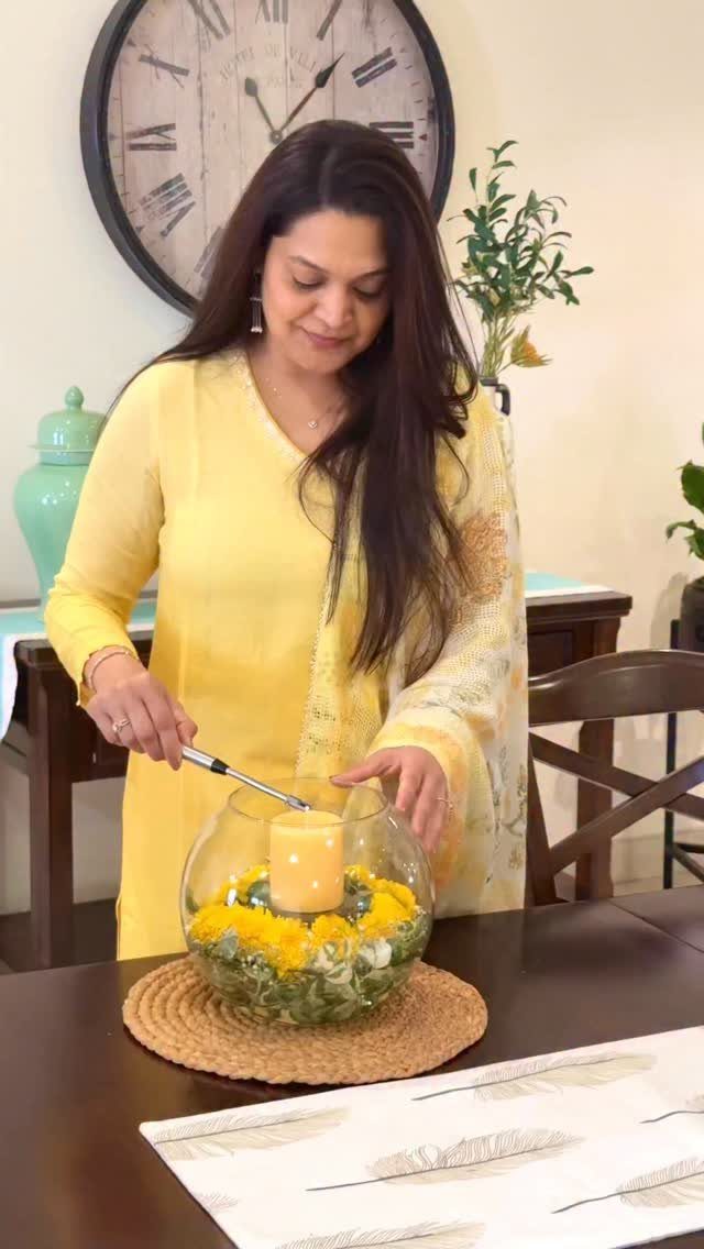 Woman arranging a glass bowl centerpiece with yellow flowers and a candle.