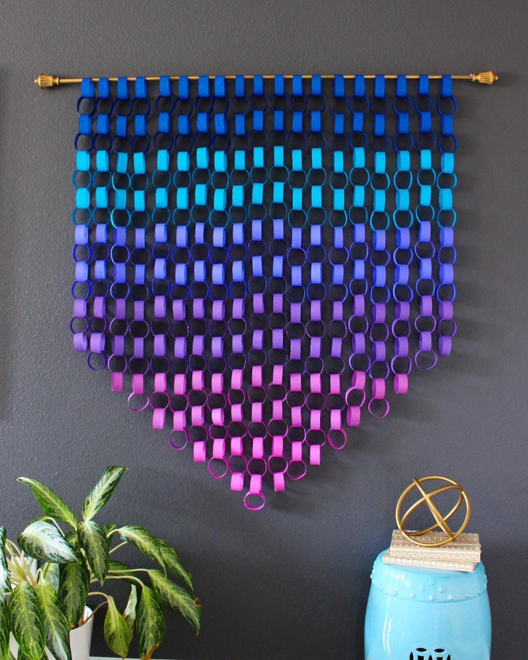 Colorful paper chain wall hanging in a blue to pink gradient on grey wall